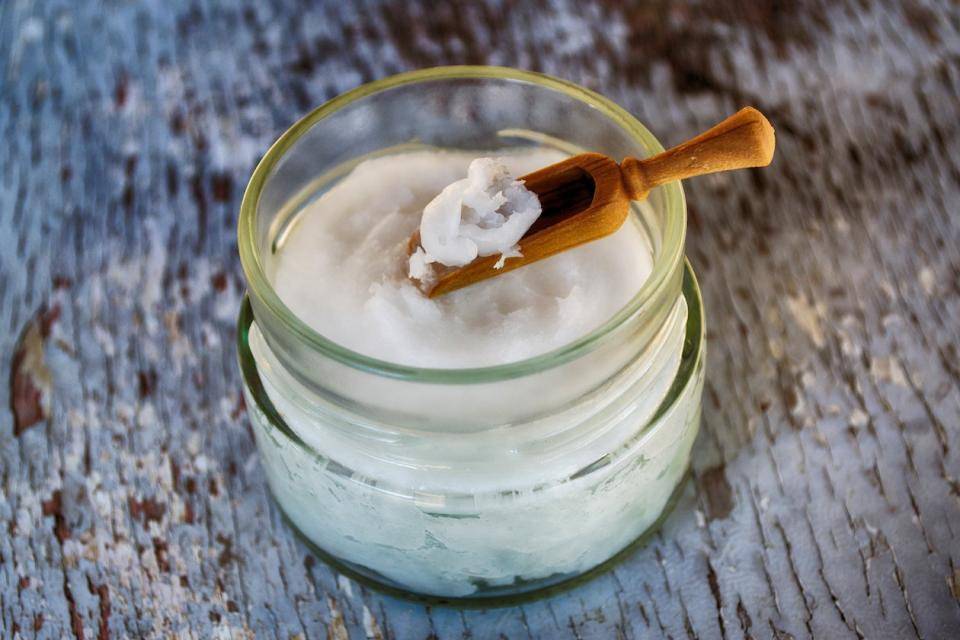 A jar of solid coconut oil with a small wooden spoon