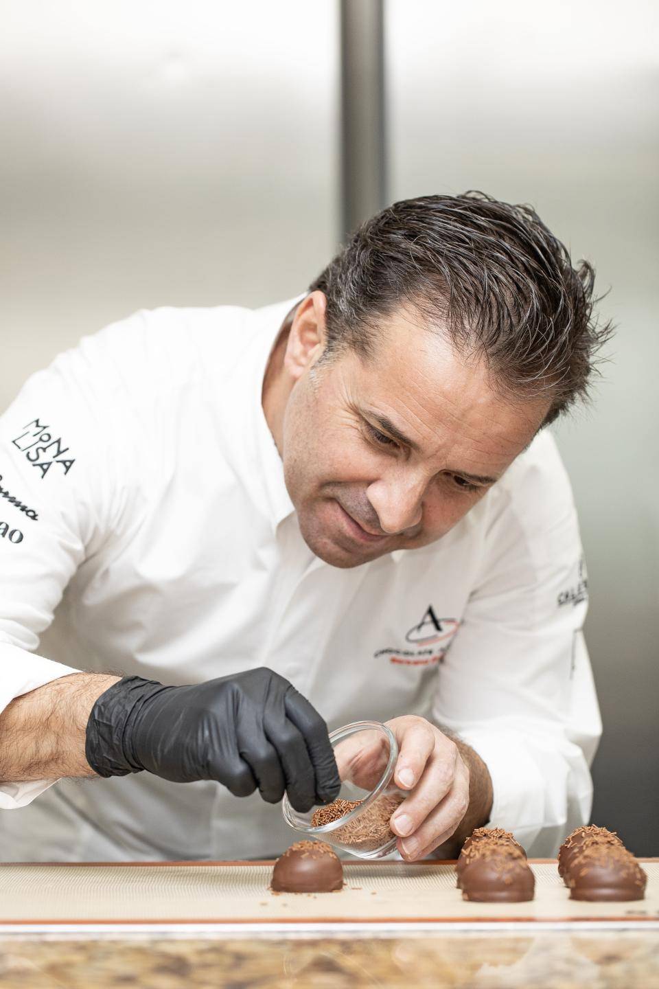 chef visto de frente com dolmã e luvas pretas finalizando receita de chocolate