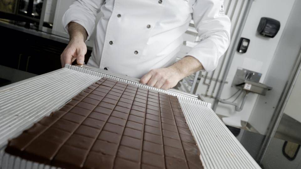 A chef prepares to separate a cut framed ganache