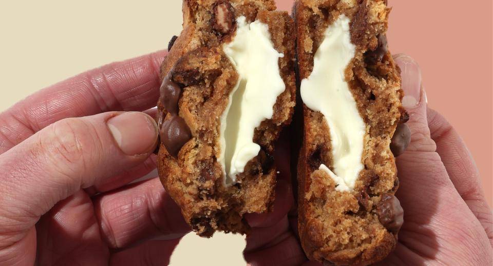 a pair of hands holding a cookie that has been broken in half, revealing a filling