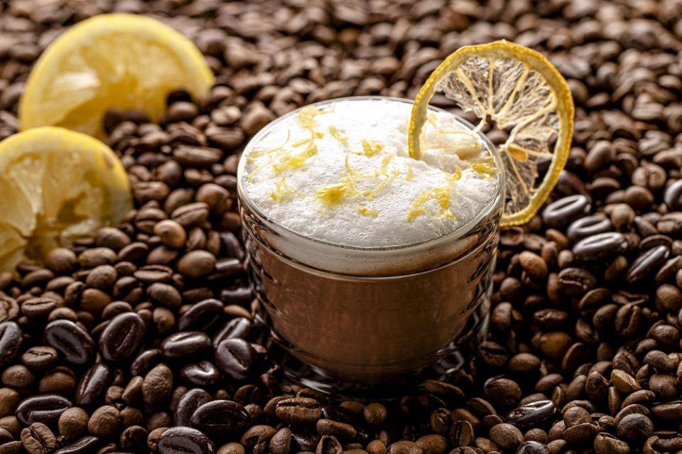 Coffee in a glass cup with handle on white tabletop with white background, coffee beans spilled at base of cup