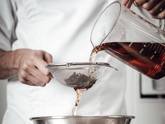 A chef pouring tea through a strainer